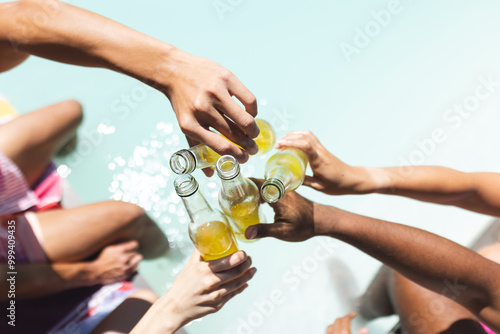 Toasting with beer bottles, diverse friends enjoying poolside hangout in summer, at home