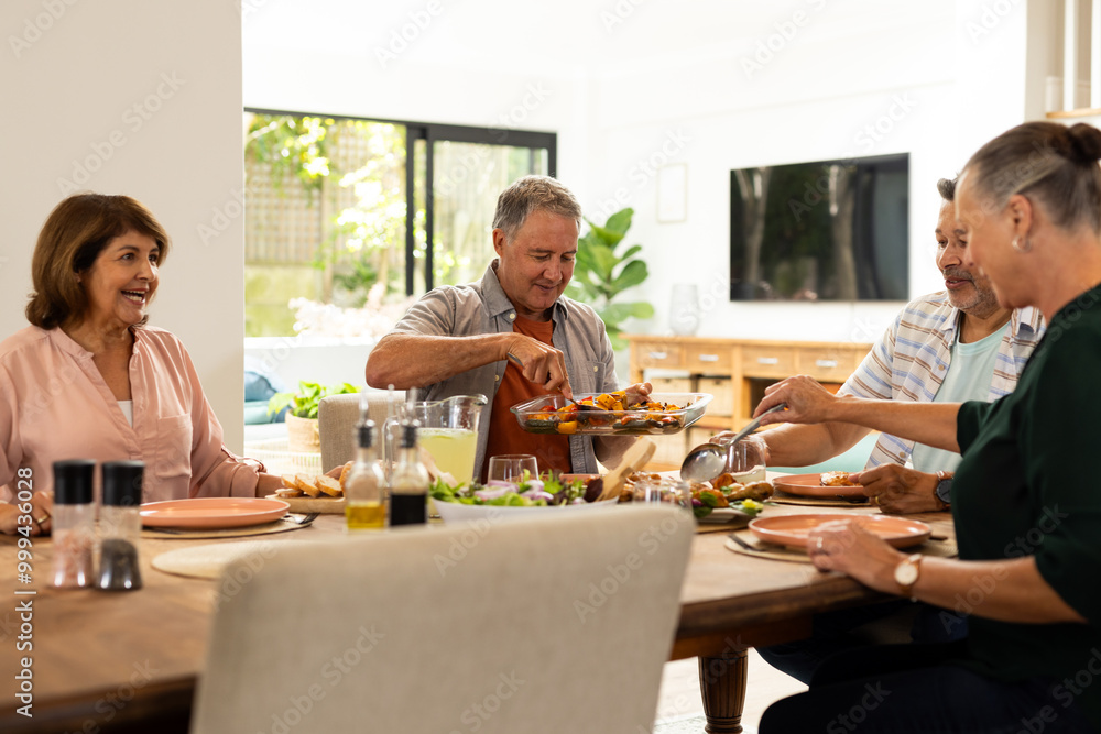 Serving food at dining table, senior diverse friends enjoying meal together indoors, at home Serving food at dining table, senior diverse friends enjoying meal together indoors, at home