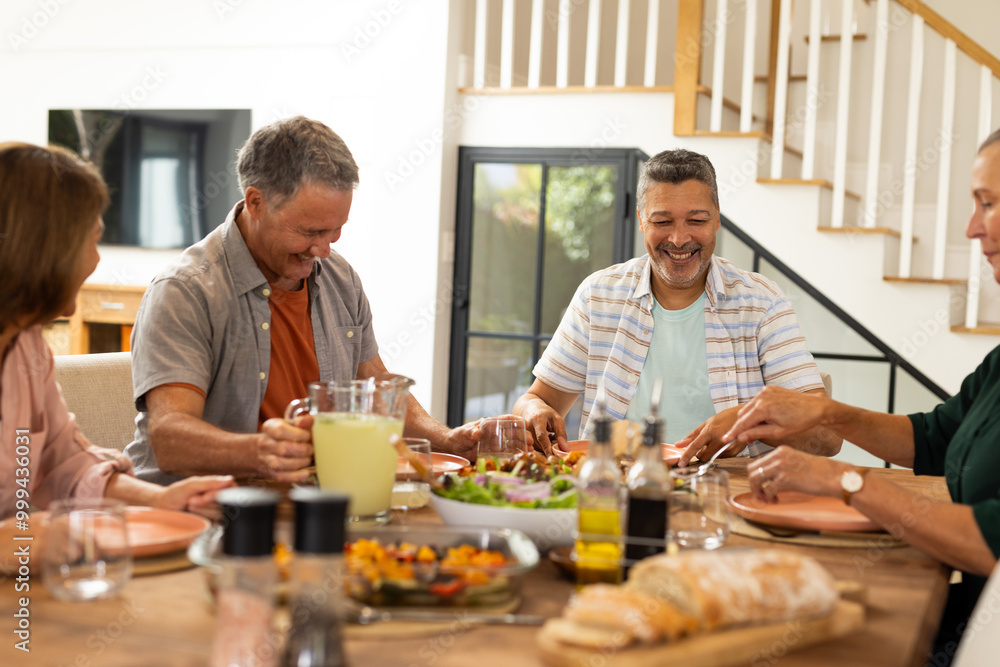Eating lunch together, senior diverse friends laughing and enjoying meal at dining table, at home Eating lunch together, senior diverse friends laughing and enjoying meal at dining table, at home