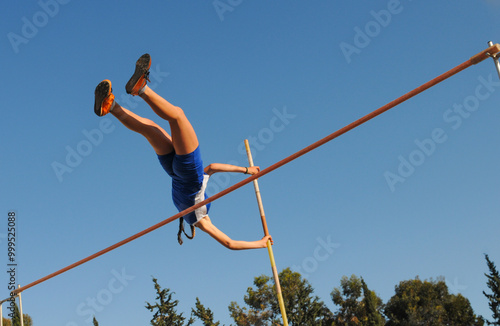Female pole vaulter clearing the bar under blue sky