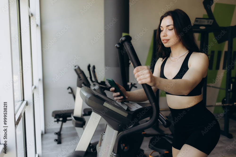 Fototapeta premium Beautiful young woman doing cardio on a stationary bike while smiling