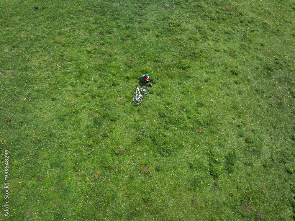 Aerial view of woman riding mountain bike on beautiful flowering grassland mountain top Aerial view of woman riding mountain bike on beautiful flowering grassland mountain top