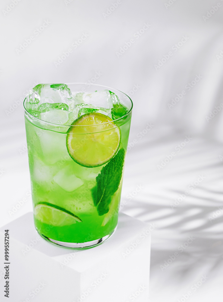 Refreshing green cocktail with lime and mint standing on white cube Refreshing green cocktail with lime and mint standing on white cube
