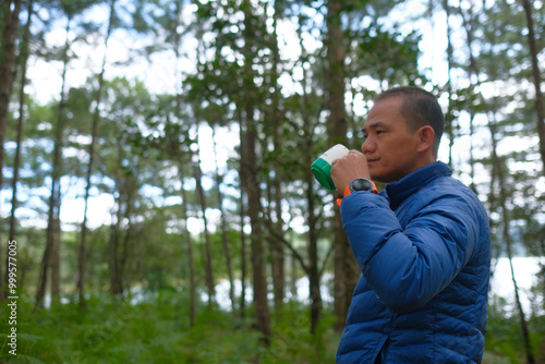 Adult asian man drink coffee in pine forest on camping trip. Royalty high-quality free best stock of man happily savoring freedom with coffee or hot tea,camper enjoying fresh air and tranquil morning