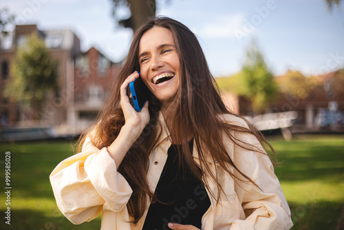 Woman, phone call and communication in park for connection, conversation or gossip. Female hold digital device and smile in nature for speaking chat or exciting news, information or discussion, joke. photo