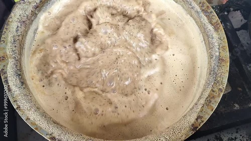 Milk Tea preparation on a gas stove in an Indian street tea stall. Close up shot of tea boiling in the streets of india. Hot tea in a sauce pan.