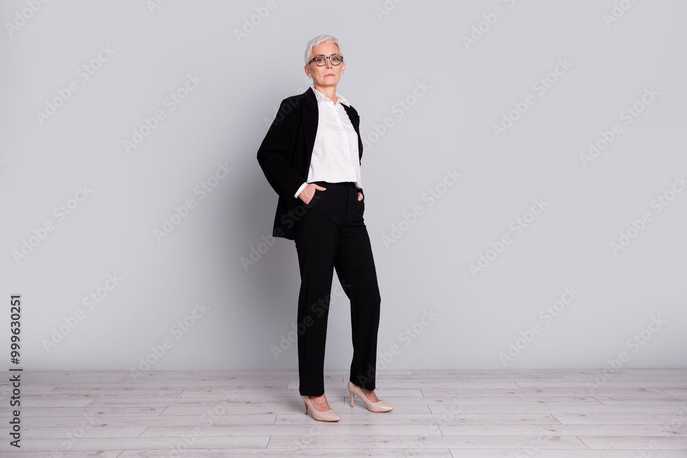 Full length photo of charming successful senior lady wear black suit office manager isolated on grey color background Full length photo of charming successful senior lady wear black suit office manager isolated on grey color background