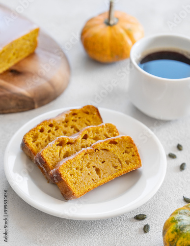 Pumpkin sweet bread or cake with icing on a plate on a light background with decorative pumpkins and a cup of coffee close up.