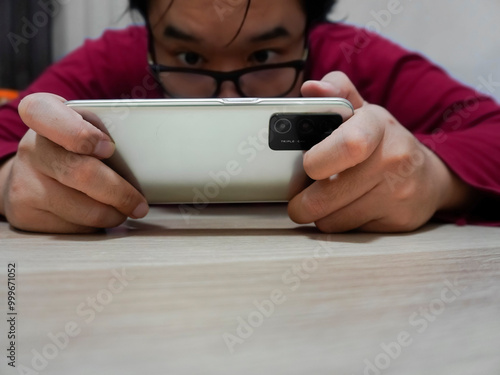 an Asian man using smartphone, playing game on his smartphone. Watching some exciting videos on his smartphone photo