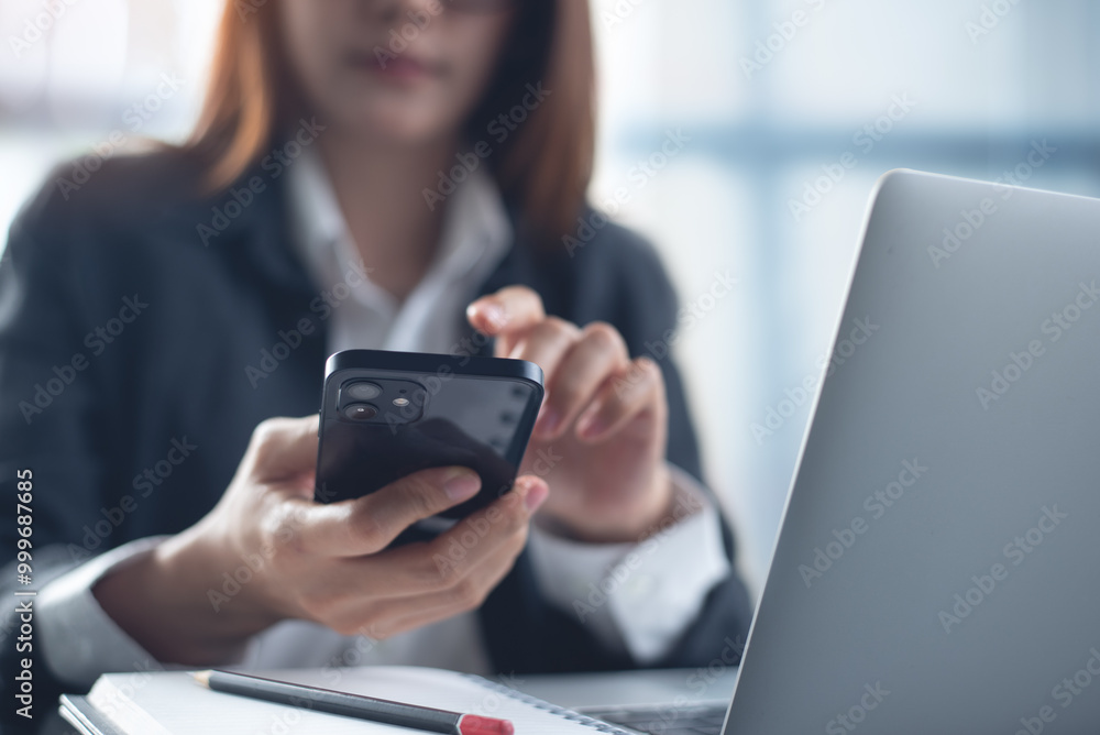 Businesswoman using mobile phone, working on laptop computer at modern office. Asian business woman using smartphone searching the information, surfing the internet, corporate business concept Businesswoman using mobile phone, working on laptop computer at modern office. Asian business woman using smartphone searching the information, surfing the internet, corporate business concept