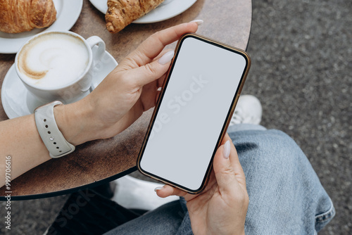 Mockup woman's hand holding using smart phone with white blank screen POV at coffee shop, mobile app design and advertising, online marketing