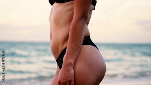 A close-up view of a woman's toned midsection in a black bikini by the sea.