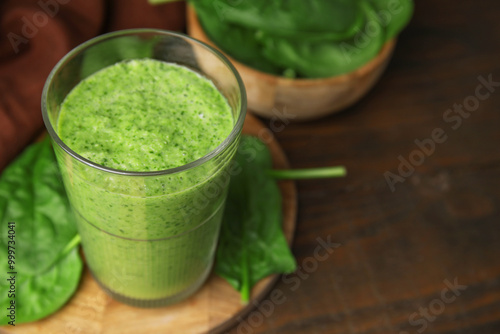 Tasty green smoothie in glass and spinach on wooden table, closeup. Space for text