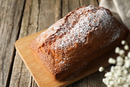 Tasty sponge cake with powdered sugar on wooden table, closeup photo