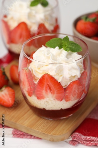 Tasty trifle dessert. Sponge cake, strawberries, jam and whipped cream in glasses on table, closeup