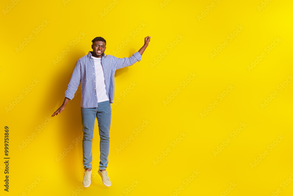 Full length photo of handsome good mood guy wear plaid shirt jumping high rising fist emtpy space isolated yellow color background Full length photo of handsome good mood guy wear plaid shirt jumping high rising fist emtpy space isolated yellow color background