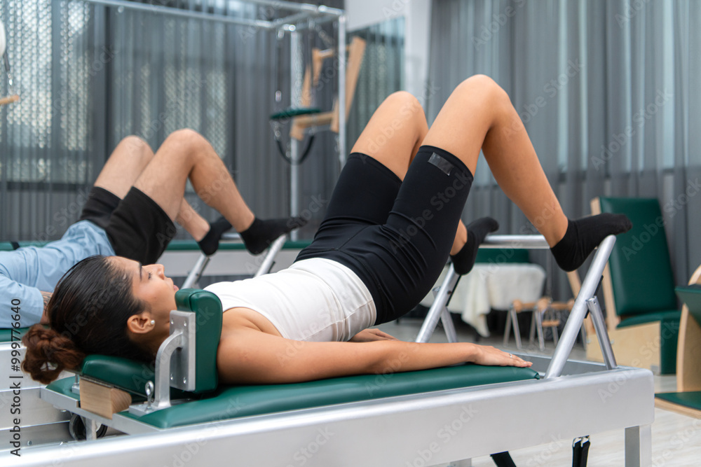A young man and a young woman are doing pilates exercises on a pilates reformer A young man and a young woman are doing pilates exercises on a pilates reformer