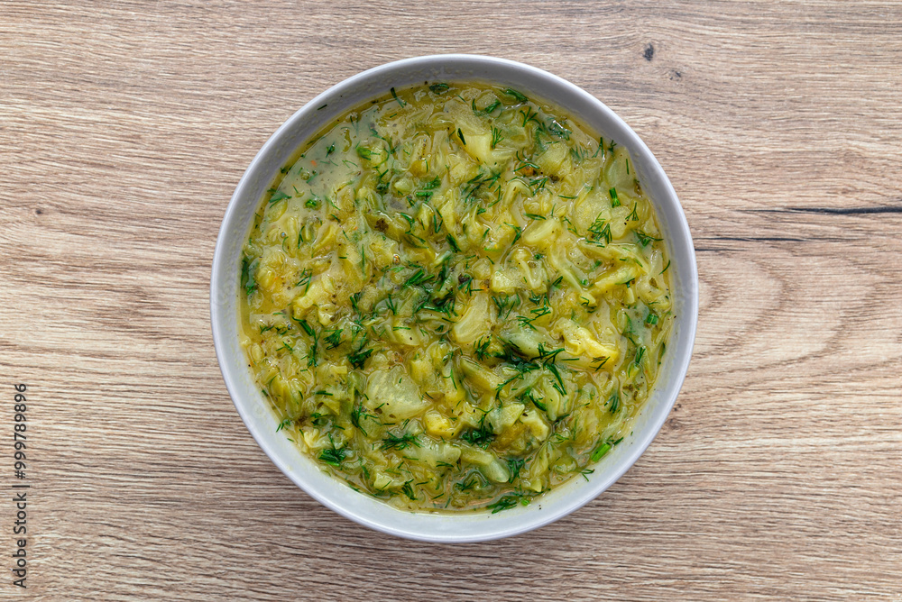 Cabbage soup made from young cabbage with parsley served in a plate, lying on the table. Cabbage soup made from young cabbage with parsley served in a plate, lying on the table.
