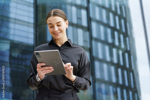 Young Professional Woman Using a Tablet Outside a Modern Office Building During the Daytime