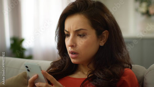 Shocked mad displeased Caucasian woman stressed nervous female girl use mobile phone chatting app texting online receiving bad message SMS smartphone error connection problem losing game at home sofa