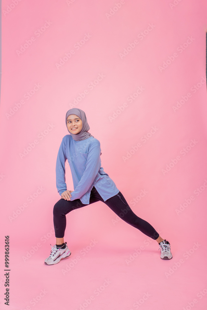 A young woman, dressed in stylish activewear, is confidently posing on a vibrant pink backdrop A young woman, dressed in stylish activewear, is confidently posing on a vibrant pink backdrop