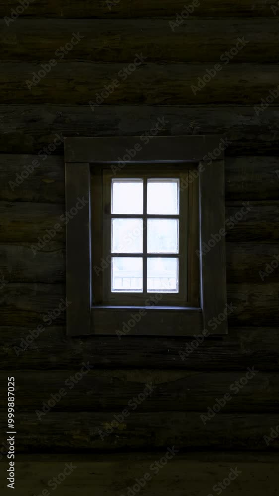 A small window in a traditional Russian wooden izba illuminates the dark log interior with soft natural light. The contrast between the warm, rough logs and the bright window creates a cozy, rustic A small window in a traditional Russian wooden izba illuminates the dark log interior with soft natural light. The contrast between the warm, rough logs and the bright window creates a cozy, rustic