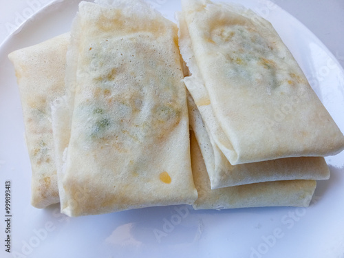 Martabak Telur Kulit Lumpia, crispy snacks filled with eggs, meat, and scallions wrapped in spring roll skin. Favorite street food eaten with green chili. before being fried on a white plate photo