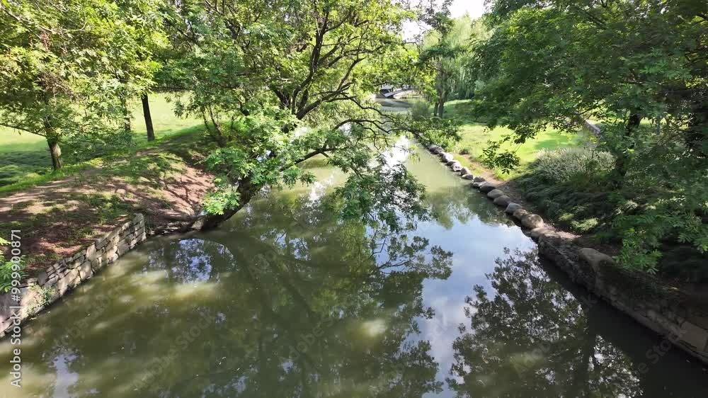 A serene, peaceful scene of a calm river, surrounded by lush green trees, their branches casting soft shadows on the water's surface. Beautiful environment in an urban park. A serene, peaceful scene of a calm river, surrounded by lush green trees, their branches casting soft shadows on the water's surface. Beautiful environment in an urban park.