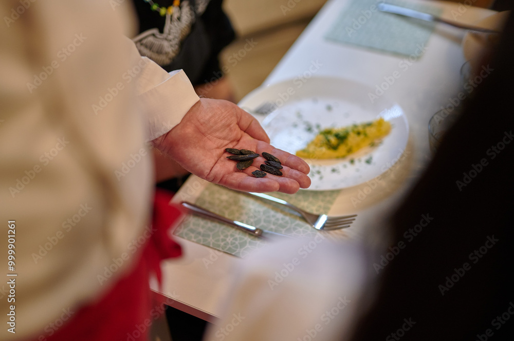 Chef Presenting Exotic Seeds to Diners During a Tasting Experience in a Warm, Ambient Light Setting Over a Prepared Dish`