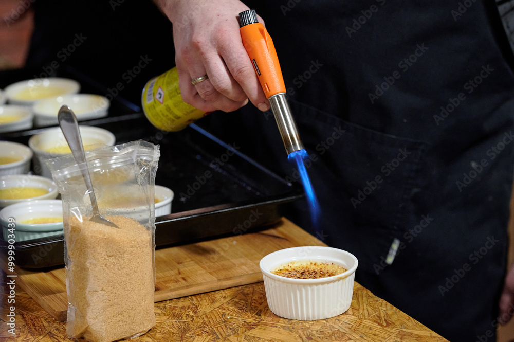 Chef Using a Kitchen Torch to Caramelize Crème Brûlée, Captured Indoors with Warm Ambient Light During a Culinary Demonstration