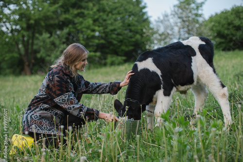 A young female farmer feeds a calf in a meadow in the village.