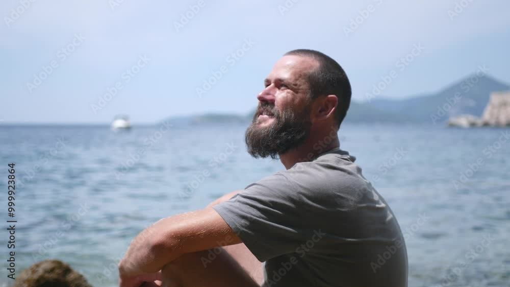 Young attractive bearded guy sits on a rock on the seashore and enjoys the beautiful view. Young bearded guy meditates on the seashore. Young attractive bearded guy sits on a rock on the seashore and enjoys the beautiful view. Young bearded guy meditates on the seashore.