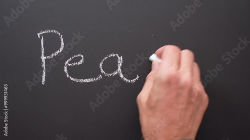 A hand writes the word peace with white chalk on a black board