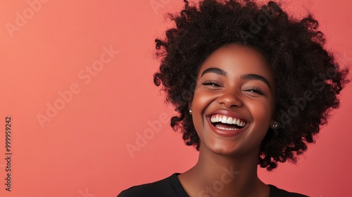 A young woman with curly black hair smiles brightly at the camera against a coral pink background.