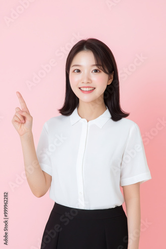 Photo of an Asian woman in a shirt standing smiling and looking at something around her. She makes a hand gesture to express her feelings, against a white background.