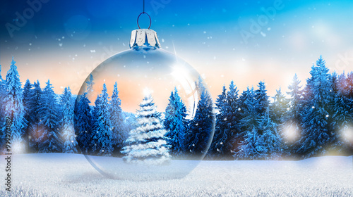 Weihnachtskugel aus Glas vor verschneiter Landschaft im Hintergrund