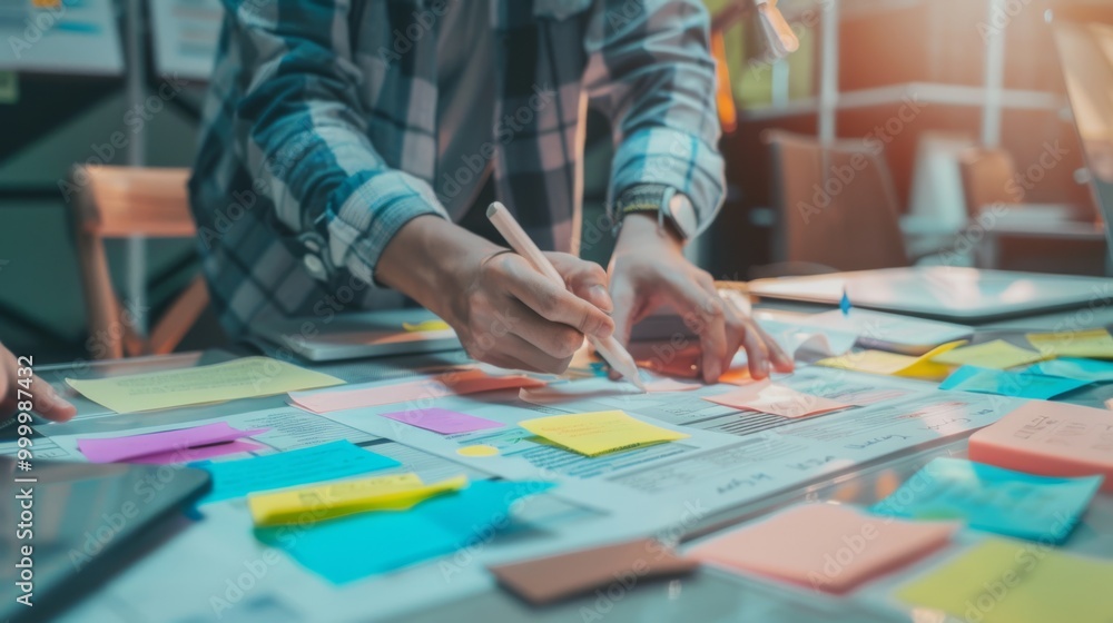 Fototapeta premium A busy workspace captures hands organizing colorful sticky notes, highlighting a collaborative brainstorming session.