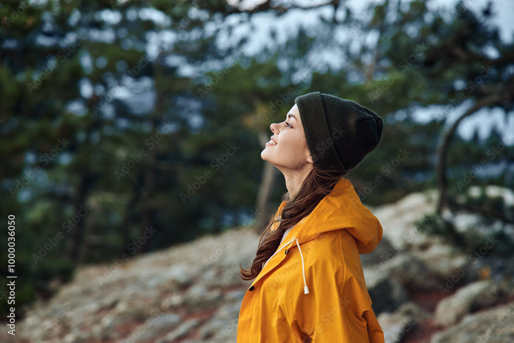 Woman in a yellow raincoat exploring nature on a rocky hill with trees in background on a rainy day Woman in a yellow raincoat exploring nature on a rocky hill with trees in background on a rainy day