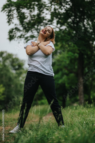 Happy woman smiling and hugging herself in a lush green park. Embracing joy and freedom in the outdoors, surrounded by nature and fresh air.