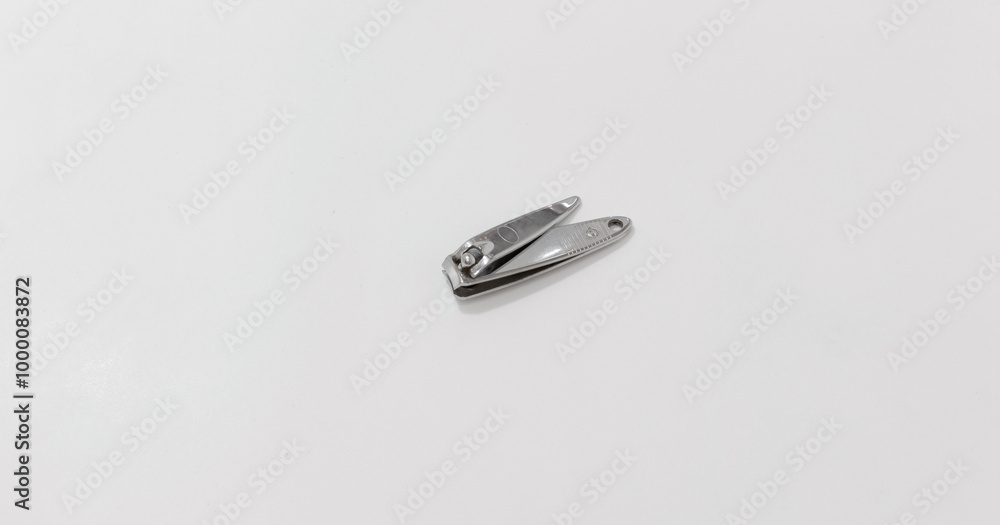 A single metal nail clipper lies on plain white surface, showcasing its simple and functional design. A single metal nail clipper lies on plain white surface, showcasing its simple and functional design.