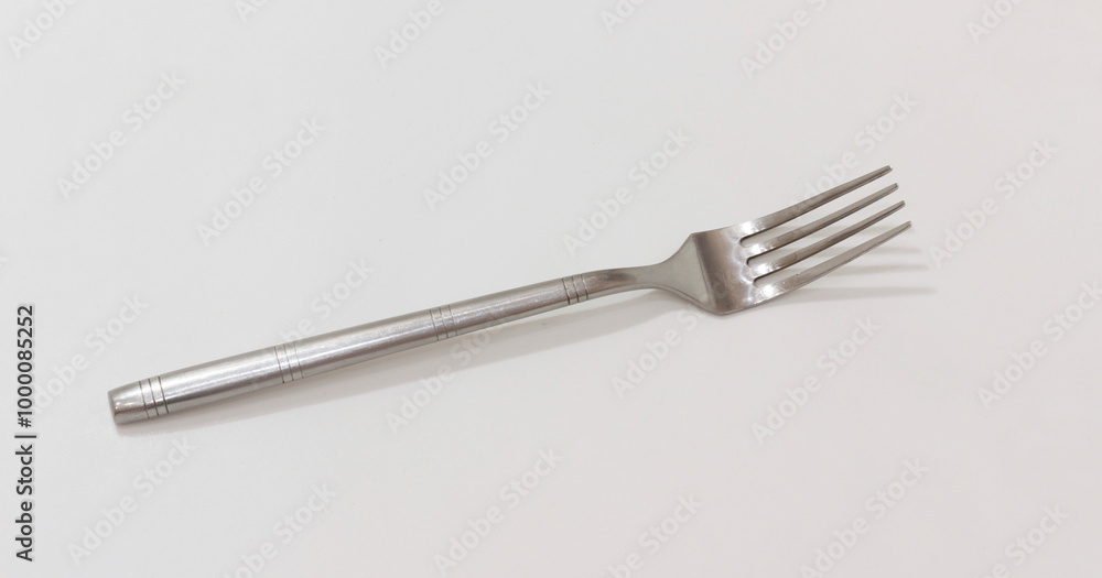 A simple stainless steel fork with four tines, resting on light colored surface, minimalistic design. A simple stainless steel fork with four tines, resting on light colored surface, minimalistic design.