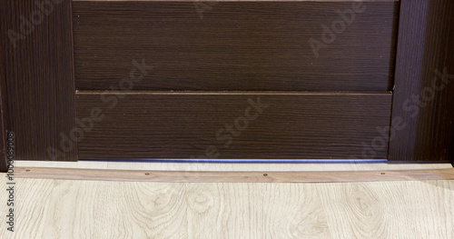 A close up of brown wooden door with floor threshold on light wooden flooring.