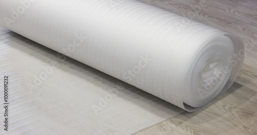 Rolled white foam underlay on wooden flooring, perfect for insulation, soundproofing, and cushioning.
