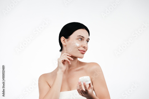 Beauty portrait of brunette woman in white towel, applies cream to the face. Skincare cleansing eco organic cosmetic spa relax concept. Free copy space for text, banner. Cosmetics advertising