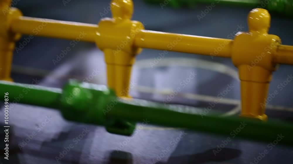 Foosball table in action with a close-up view of player rods and the ball in motion. The yellow and green figures show fast-paced gameplay in an intense tabletop soccer match Foosball table in action with a close-up view of player rods and the ball in motion. The yellow and green figures show fast-paced gameplay in an intense tabletop soccer match