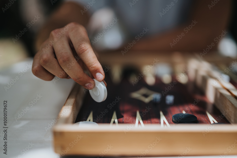 Fototapeta premium A hand strategically plays backgammon on a wooden board, highlighting focus and strategy in a traditional board game setting.
