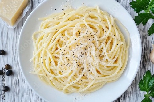 Steaming plate of spaghetti cacio e pepe seasoned with ground black pepper and grated parmesan cheese, top view