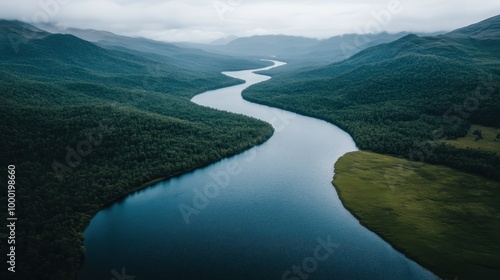 An aerial capture of a sinuous river threading its way through verdant hills, enshrouded in a mist that imparts an ethereal quality to the tranquil and pristine landscape.