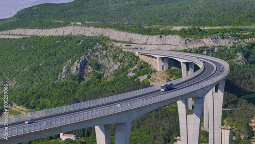 AERIAL: Truck hauling cars drives along the breathtaking Crni Kal viaduct. Spectacular flying shot of the busy Crni Kal viaduct on a sunny summer day in rural Slovenia. Highway bridge crossing karst.