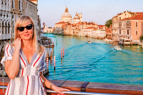 A stunningly beautiful woman poses gracefully beside the iconic Grand canal of Venice, capturing a perfect summer evening